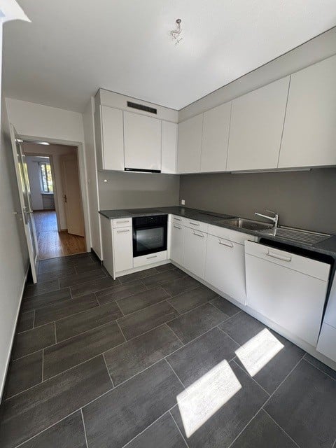 Modern kitchen with white cabinets, dark grey countertops, and dark grey tiled flooring. Features include a sink, faucet, oven, and dishwasher.