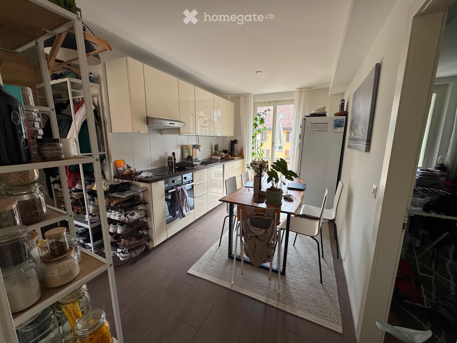 Modern kitchen with white cabinets, stainless steel appliances, a dining table with chairs, and a potted plant near the window.