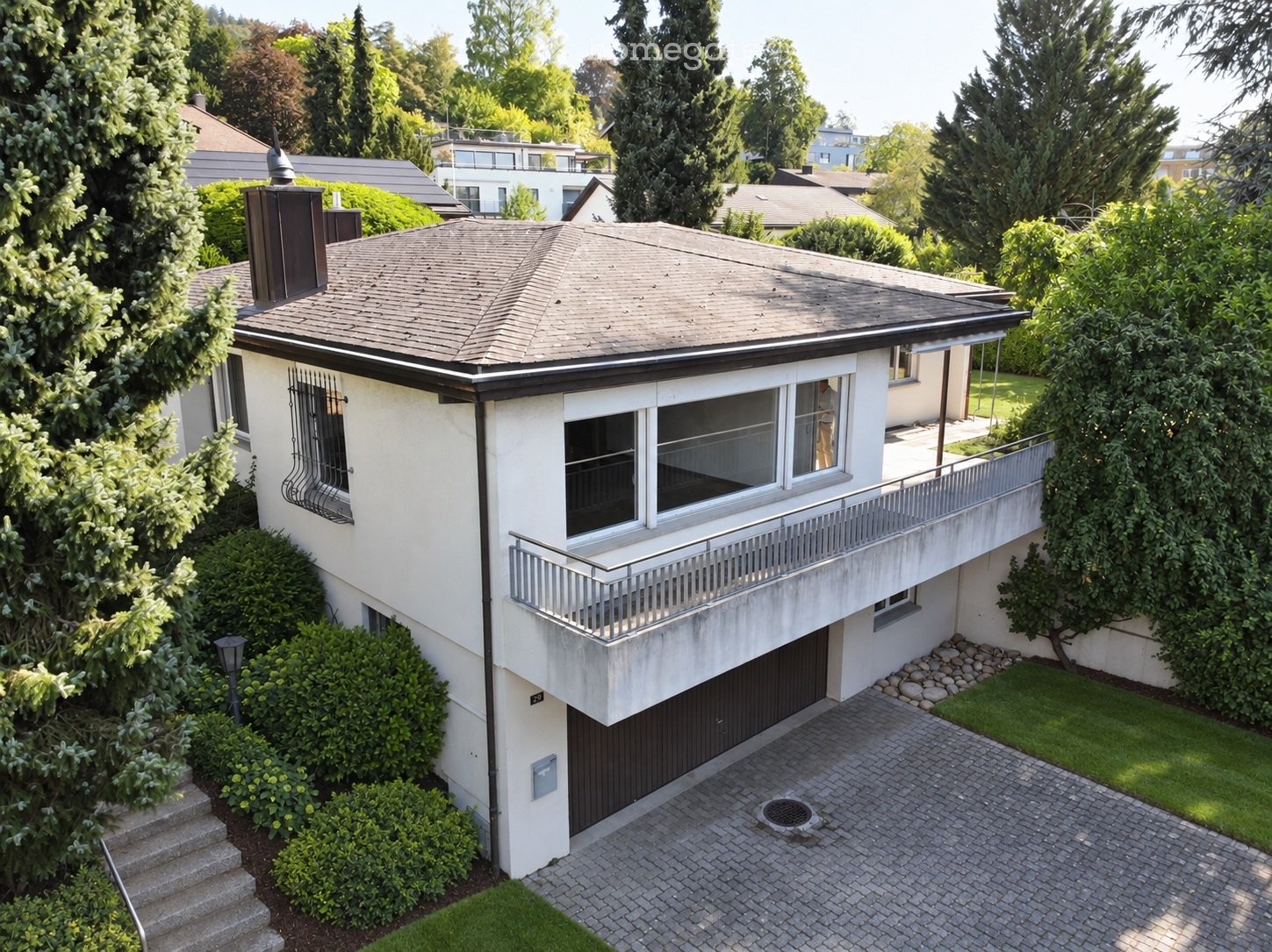Two-story house with a flat roof, white exterior, garage, balcony, and surrounding greenery.