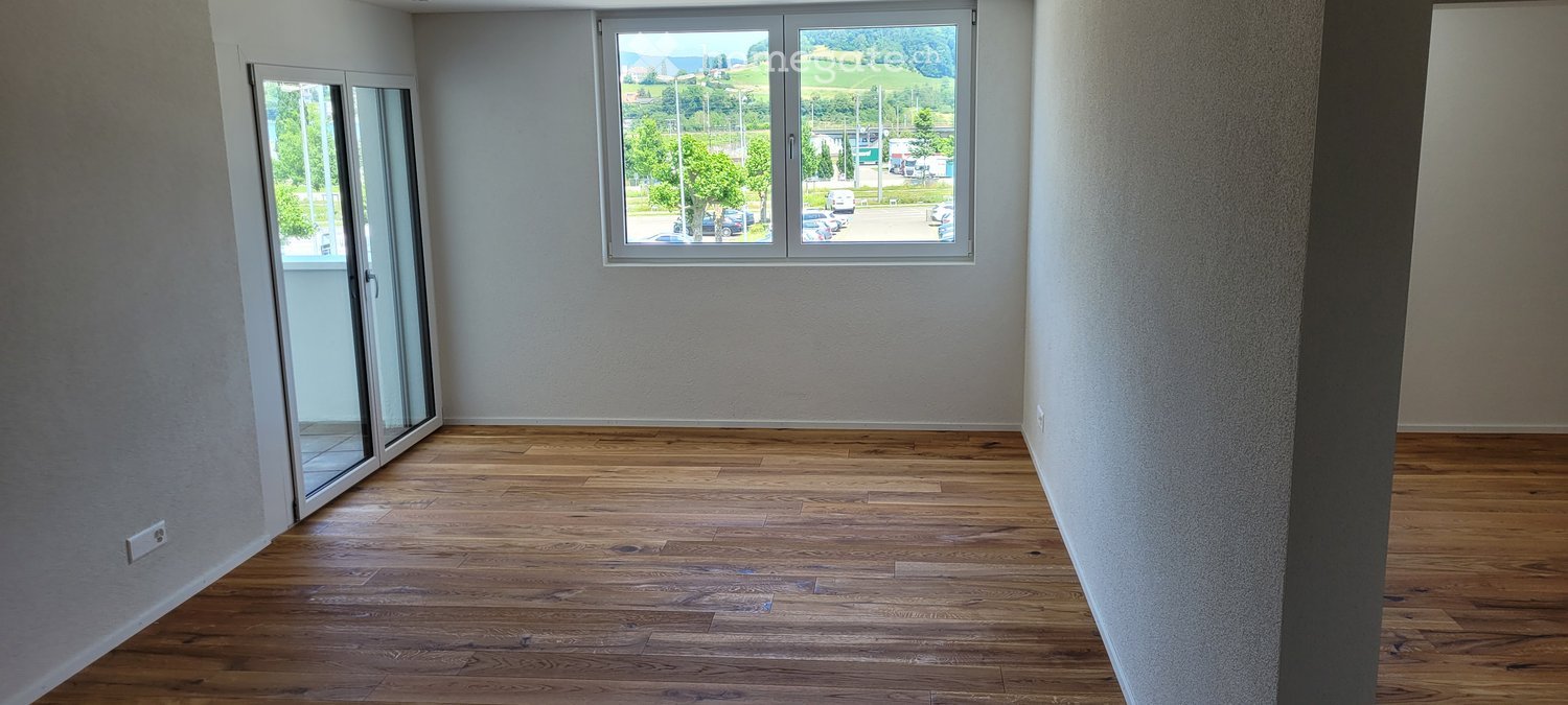 Empty room with wooden flooring, large windows, and a sliding glass door leading to a balcony.