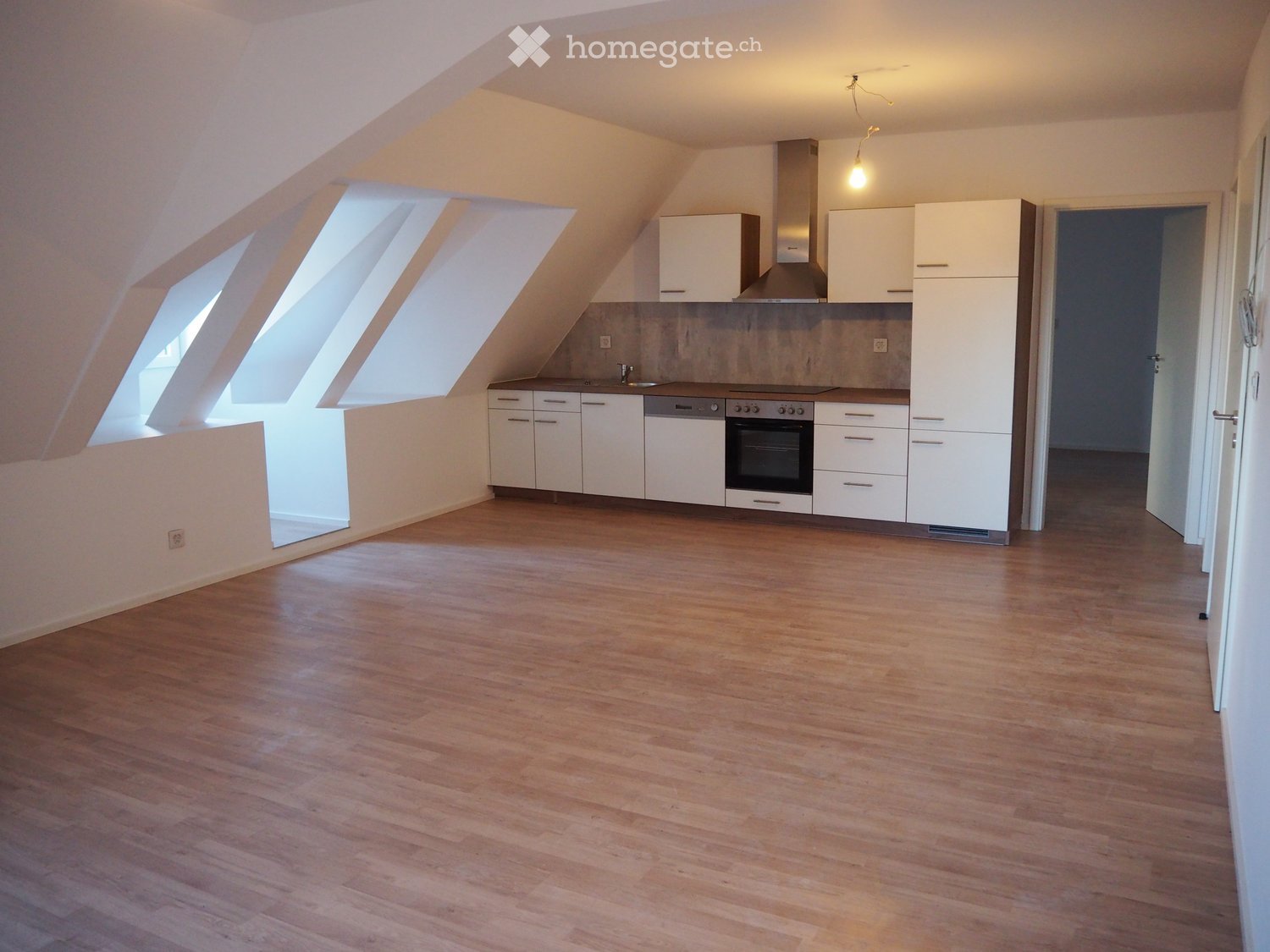 Empty attic room with wooden flooring, white kitchen cabinets, and large skylight windows.
