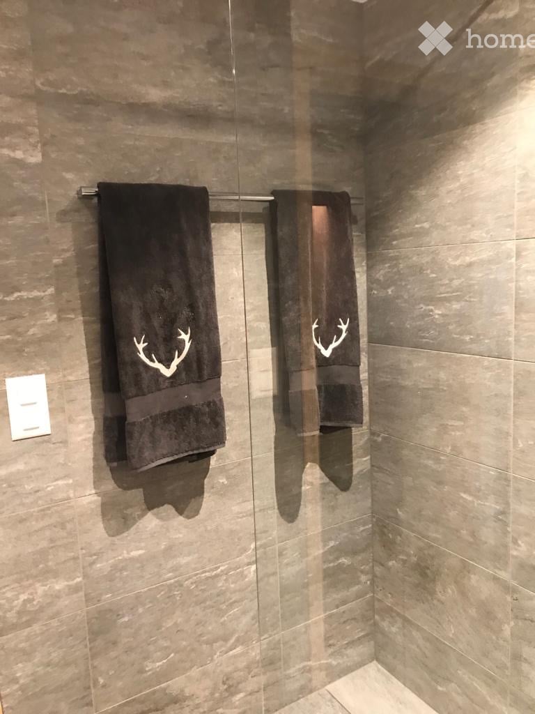 Modern bathroom with dark brown tiles, glass shower enclosure, and two black towels with white deer antler designs hanging on a rack.