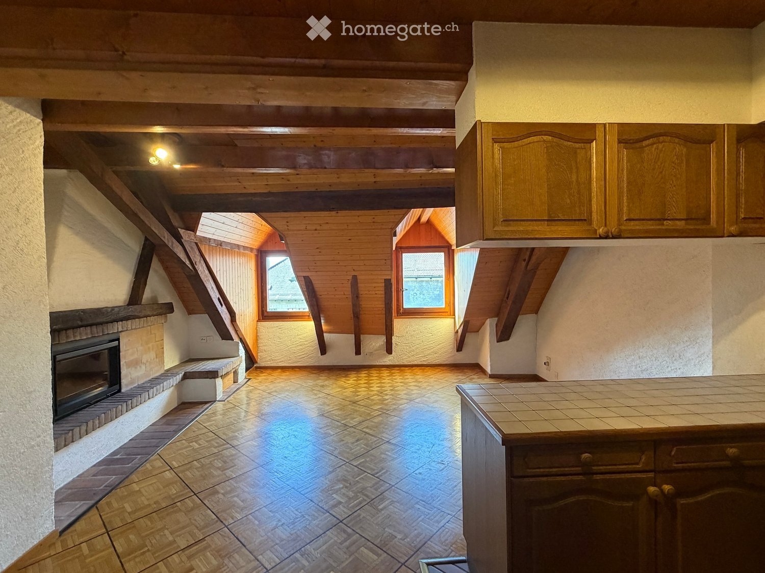 A cozy, well-lit room with wooden beams, a fireplace, and built-in cabinets. The space features a tiled floor and large windows allowing natural light to fill the room.