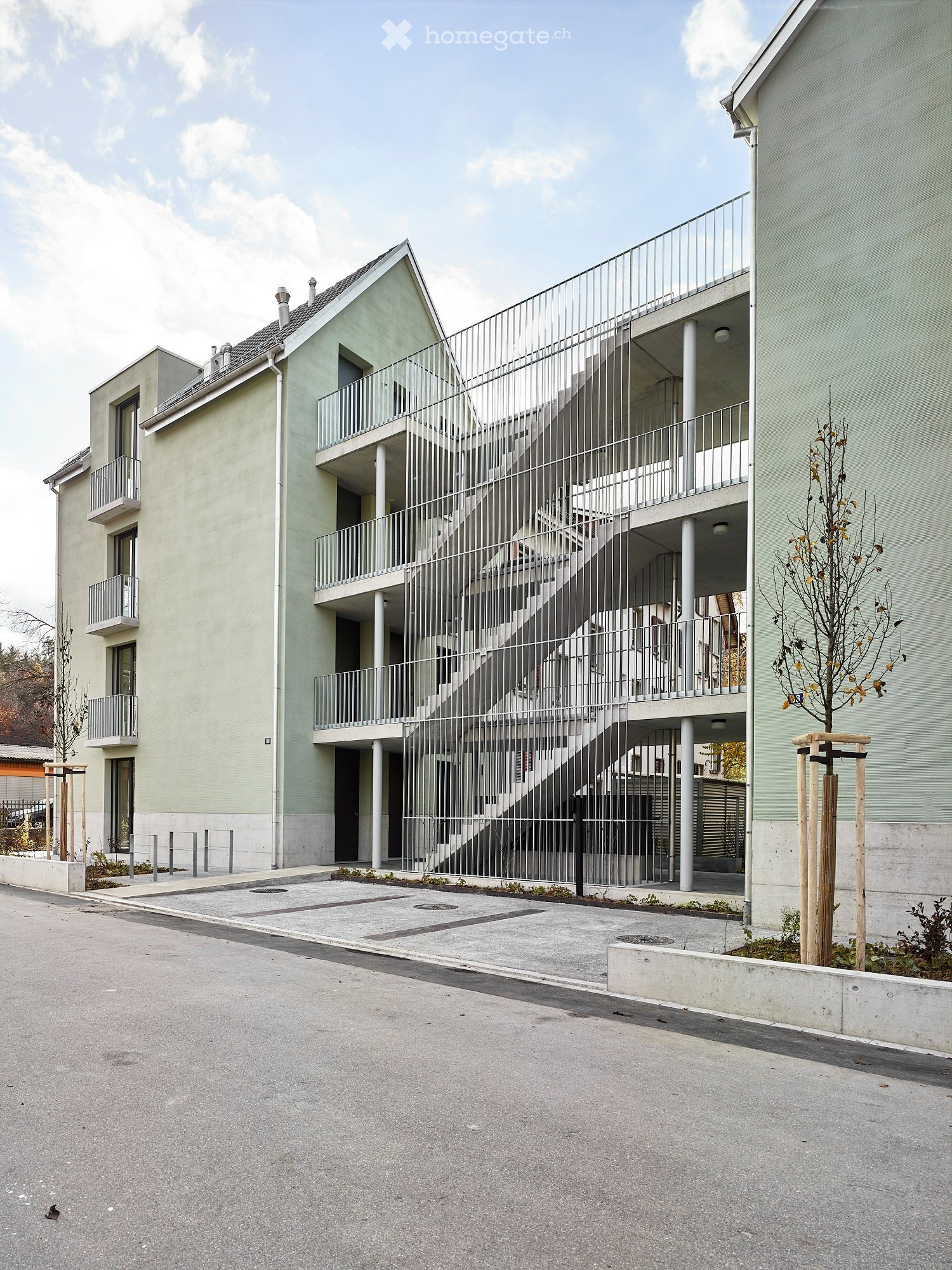 Modern apartment building with balconies, spiral staircase, and parking area