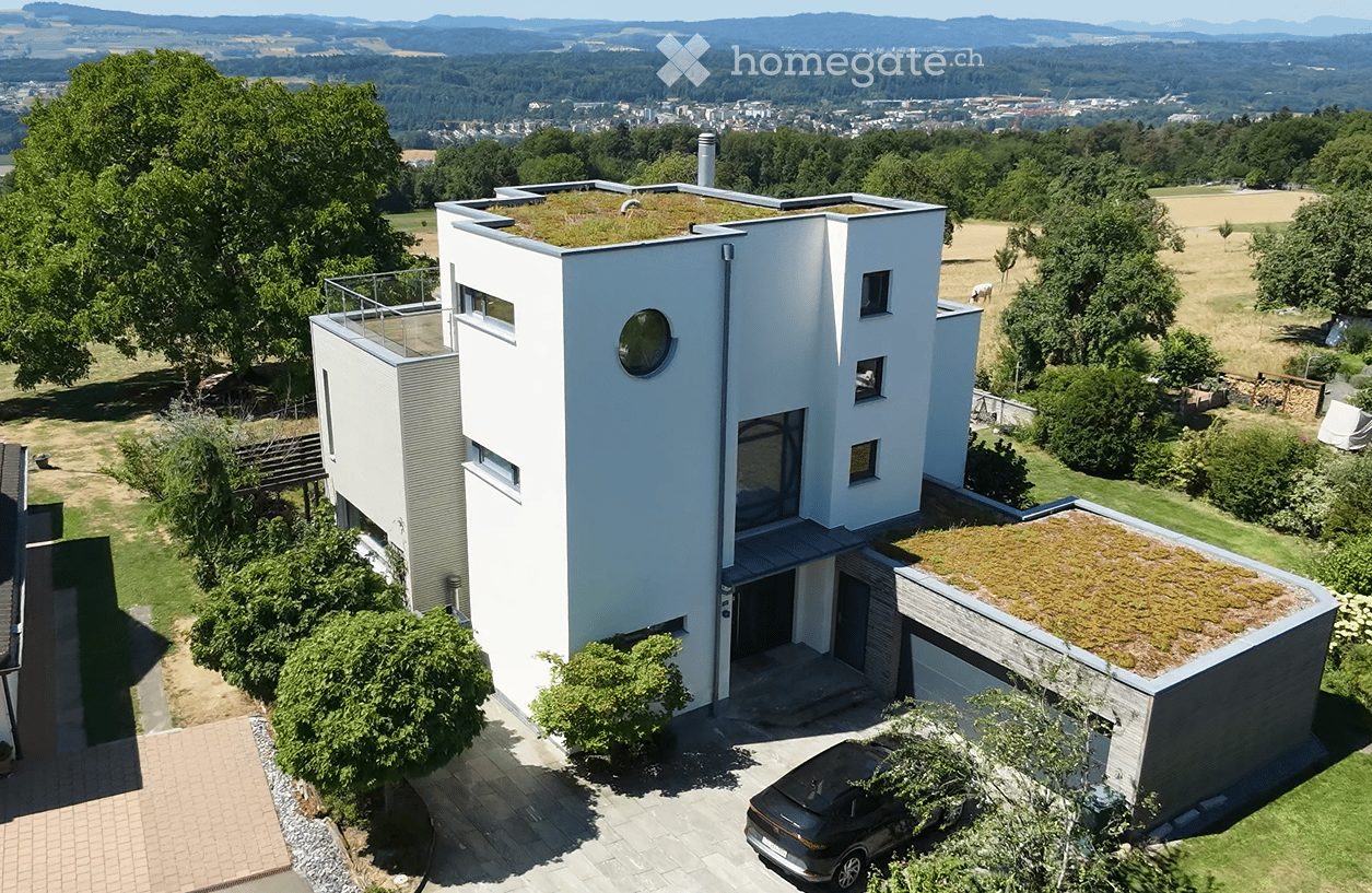 Modern white house with a green roof, garage, and scenic countryside view.