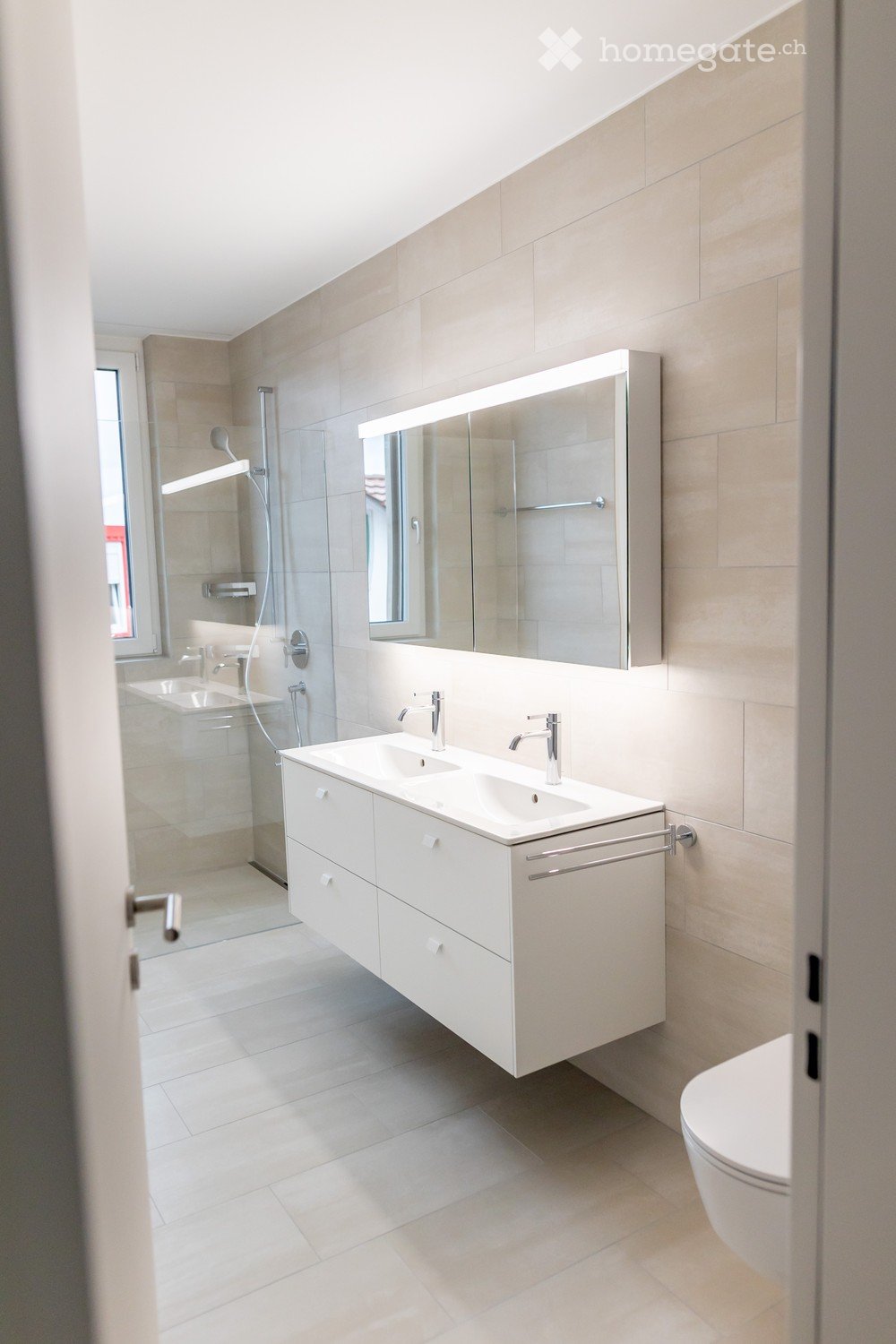 Modern bathroom with a double sink vanity, large mirror, toilet, and glass-enclosed shower area.