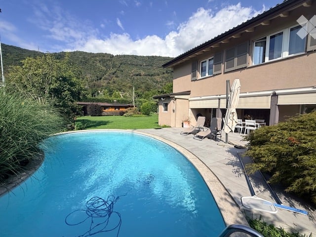 Private outdoor area with a swimming pool, lounge chairs, and a dining set under umbrellas, surrounded by greenery and a scenic mountain view.