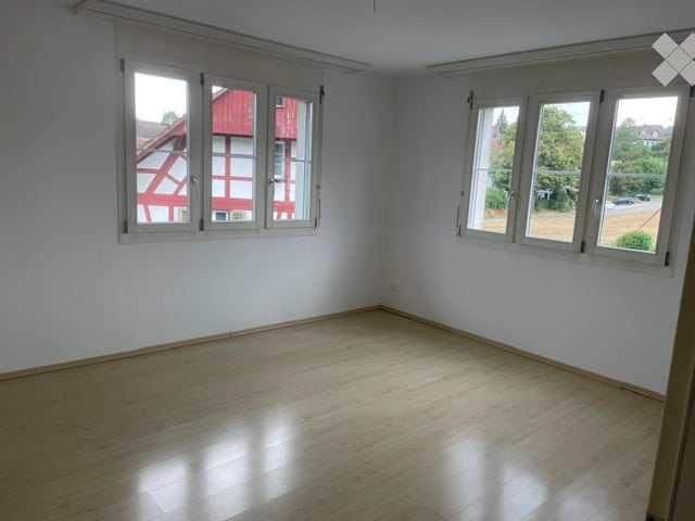Empty room with wooden flooring and white walls, featuring large windows with white frames and blinds. No furniture or equipment present.