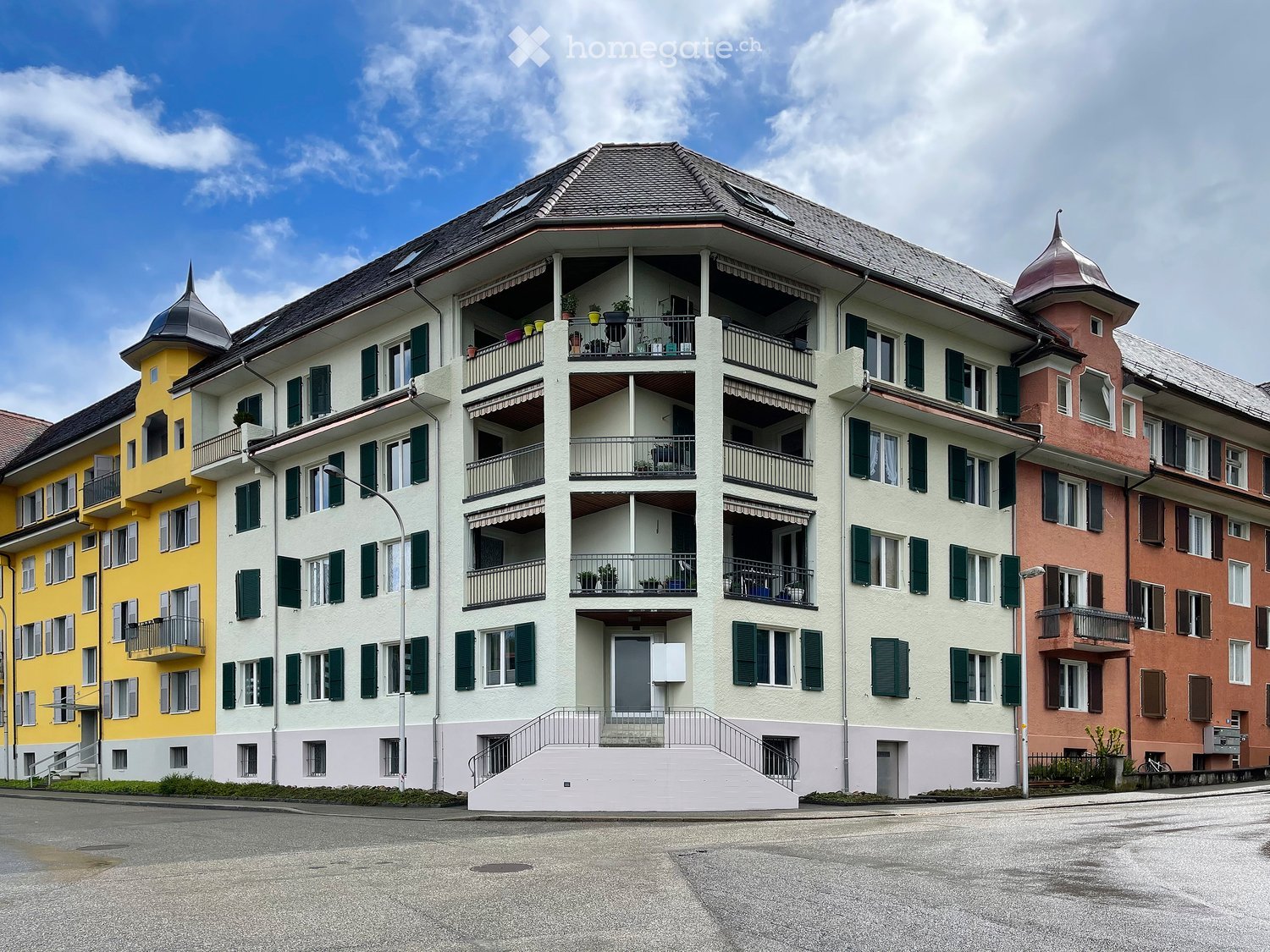 Multi-story residential building with balconies, green shutters, and decorative towers.