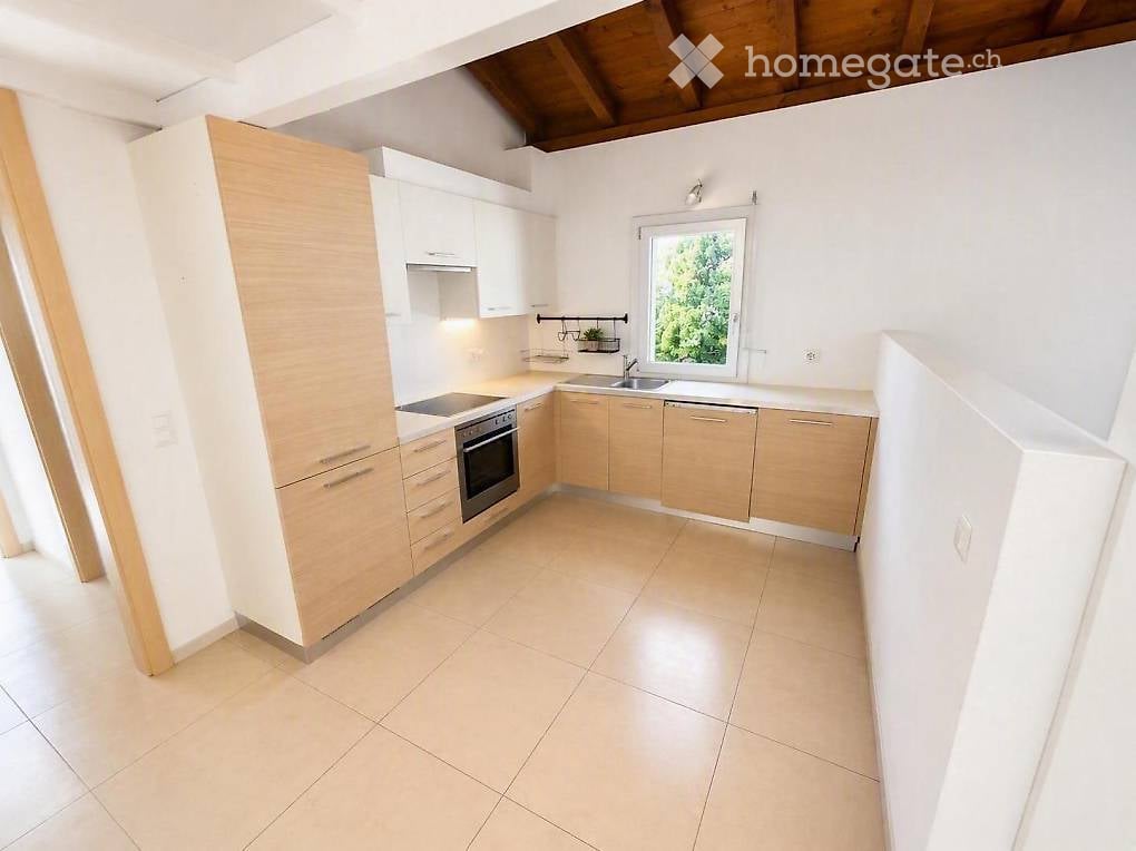 Modern kitchen with light wood cabinets, stainless steel appliances, tiled floor, and a window overlooking greenery.