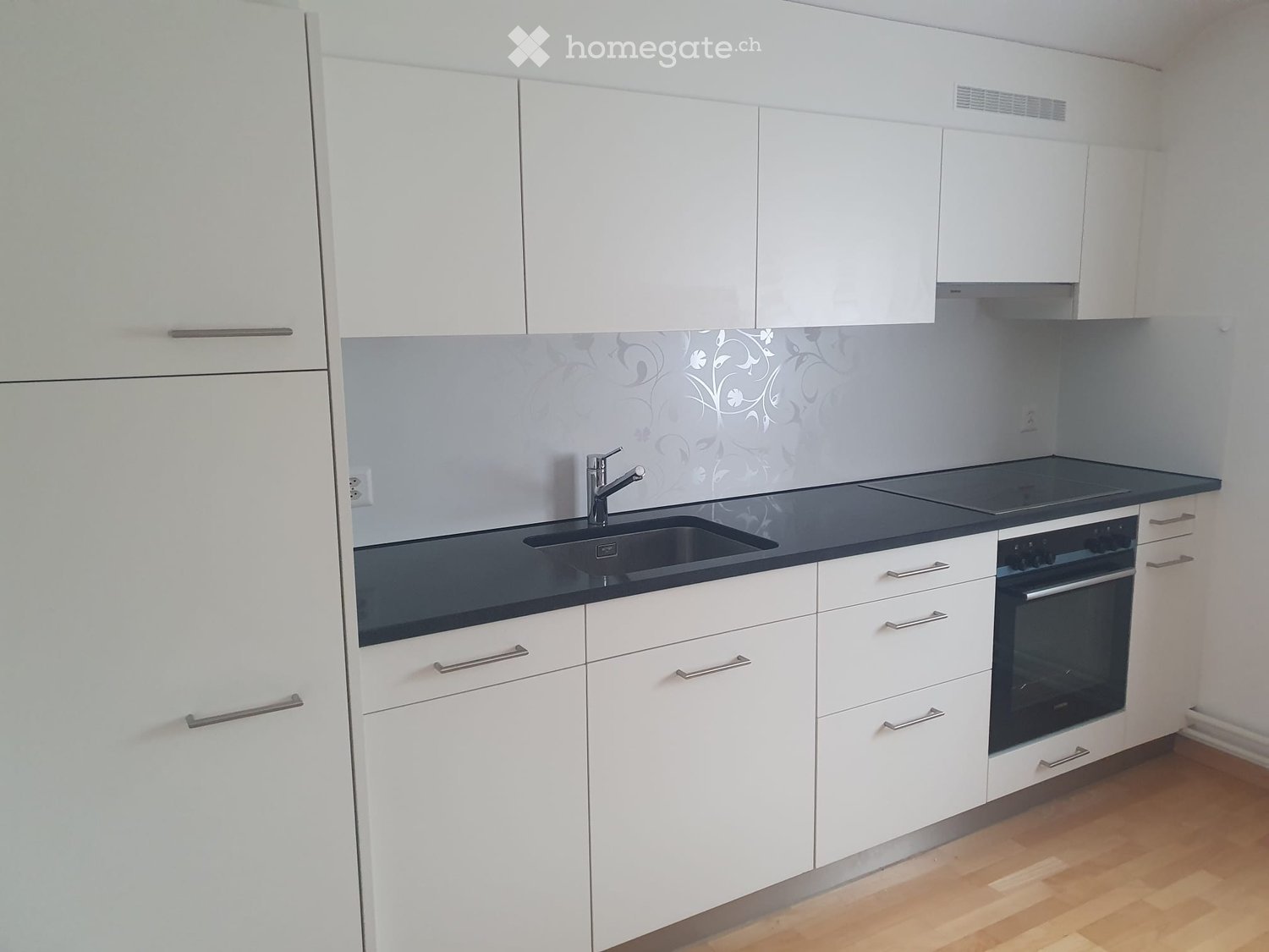 Modern kitchen with white cabinets, dark countertops, a sink with a faucet, and an oven.
