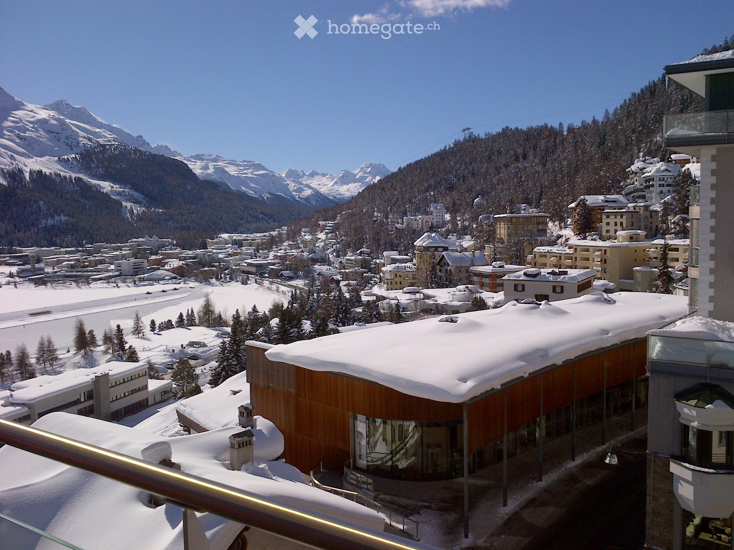 Panoramic view from a balcony overlooking a snow-covered town with mountains in the background.