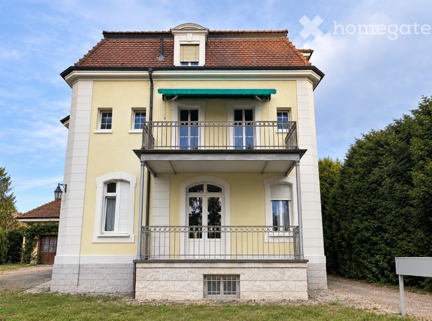 Two-story house with yellow and white exterior, red-tiled roof, multiple windows, and a balcony with metal railing.
