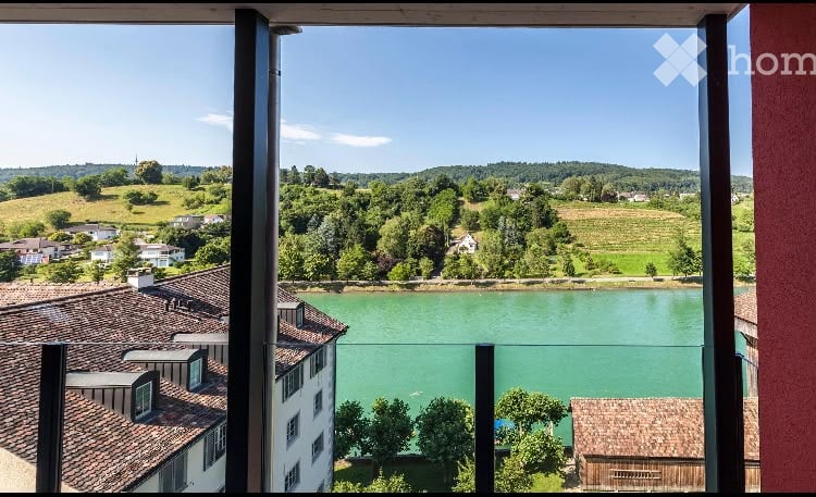 Panoramic view from a balcony overlooking a river, with surrounding greenery and houses visible.