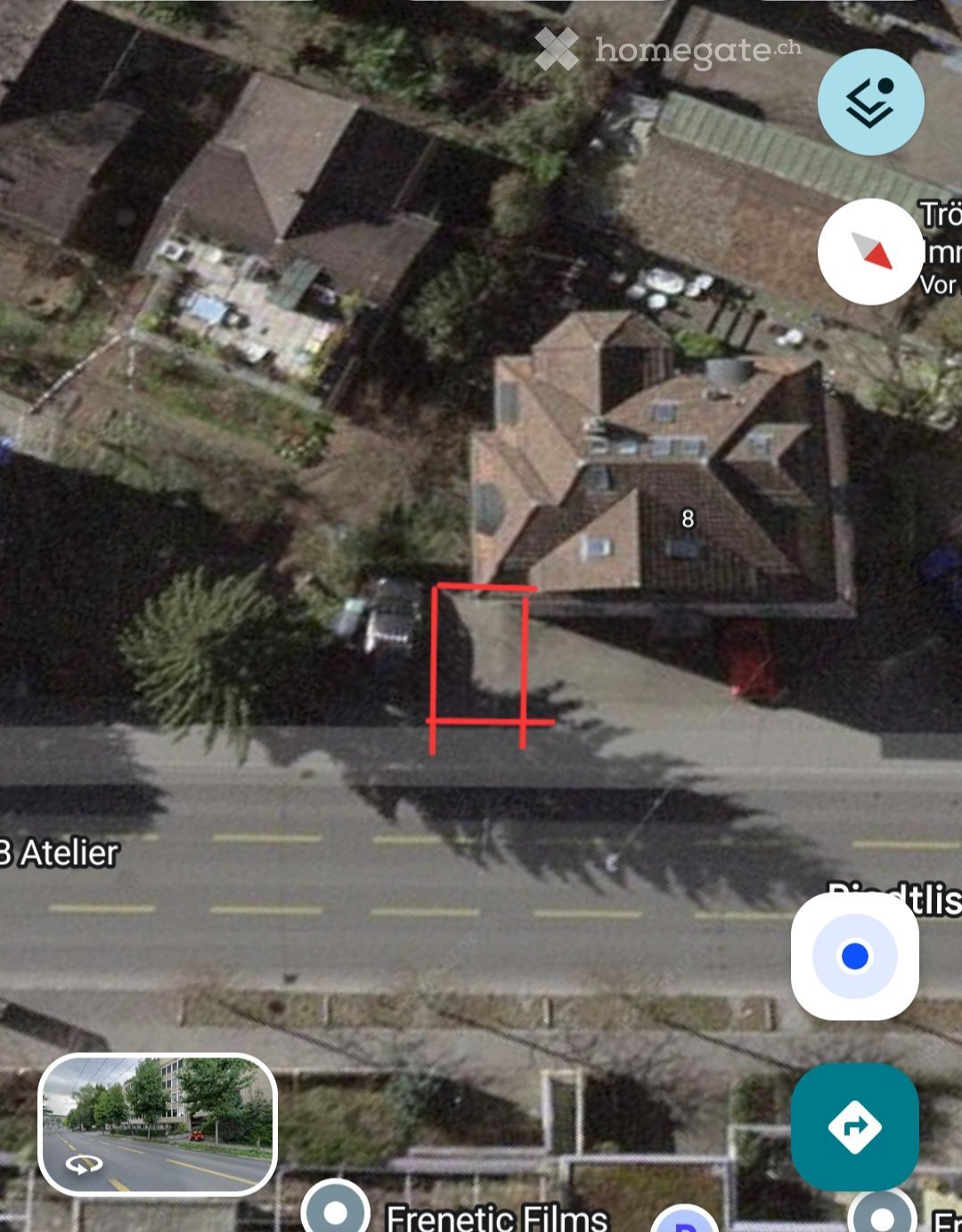 Aerial view of a residential area showing multiple houses with pitched roofs, surrounded by trees and a road.