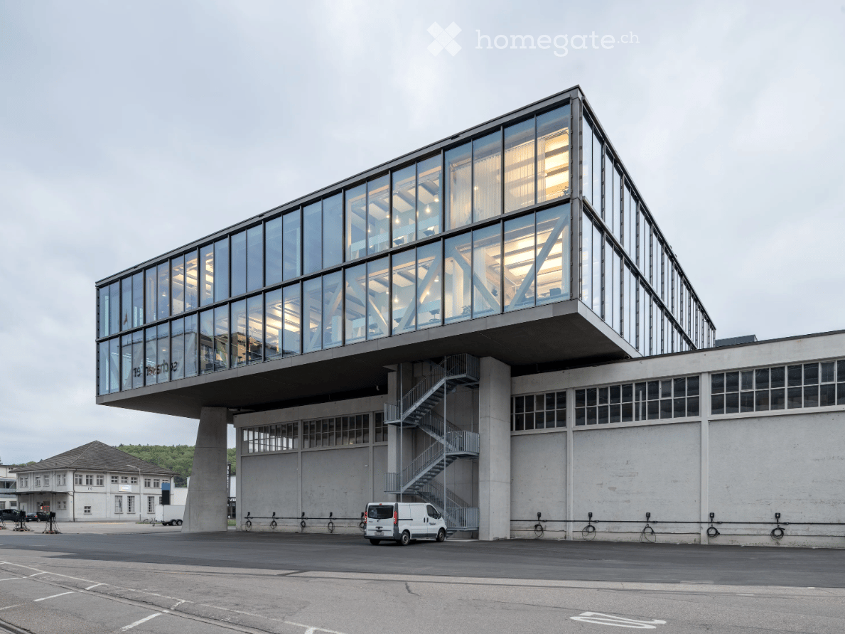 Modern building with glass facades, raised ground floor, stairs, parking lot, white van parked