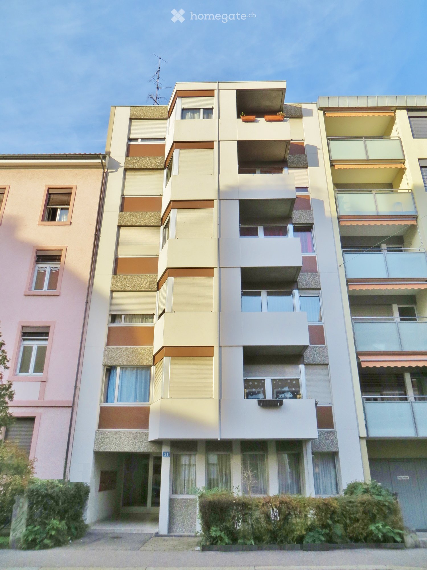 Multi-story residential building with balconies, large windows, and varied facade colors including pink, beige, and brown.