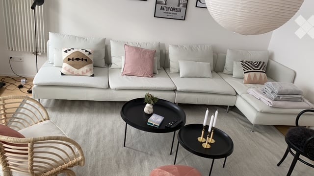 Modern living room with a white sectional sofa, decorative pillows, a black coffee table, side tables, and a wicker chair.
