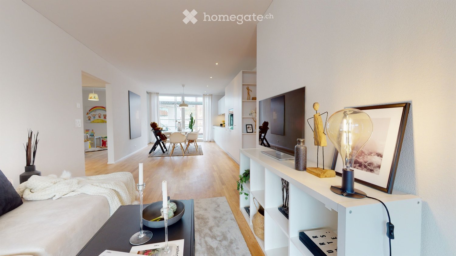 Open-plan living and dining area with modern furniture, a large TV, shelves, and decorative items.