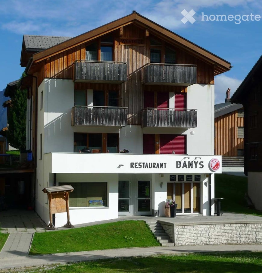 A multi-story building with a restaurant sign reading "RESTAURANT DANY'S" at the base, featuring balconies on the upper floors and a well-maintained lawn in front.