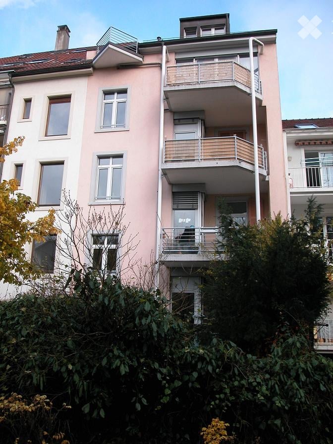 Multi-story residential building with pink facade, multiple windows, and balconies with metal railings.