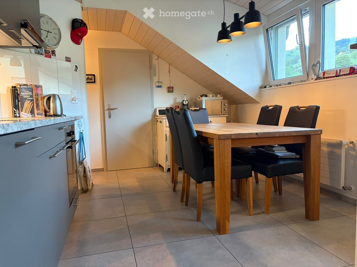 Bright kitchen with a dining area, featuring a wooden dining table with four black chairs, a refrigerator, oven, microwave, and various kitchen items on the counter.