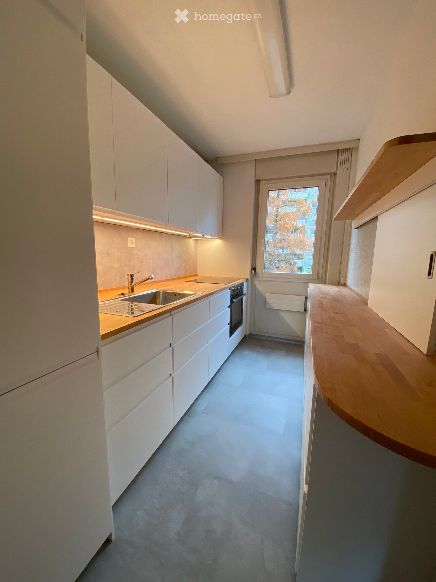 Modern kitchen with white cabinets, a sink, and an oven, featuring a wooden countertop and a window with a view of trees.