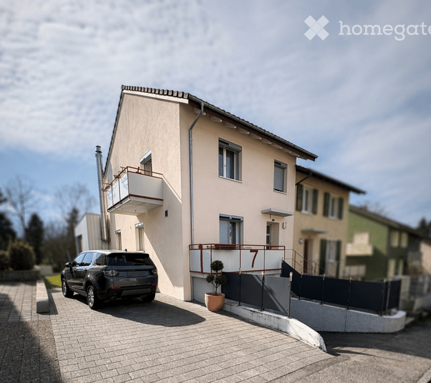 Two-story house with beige facade, white trim, balcony, and parked SUV in driveway.