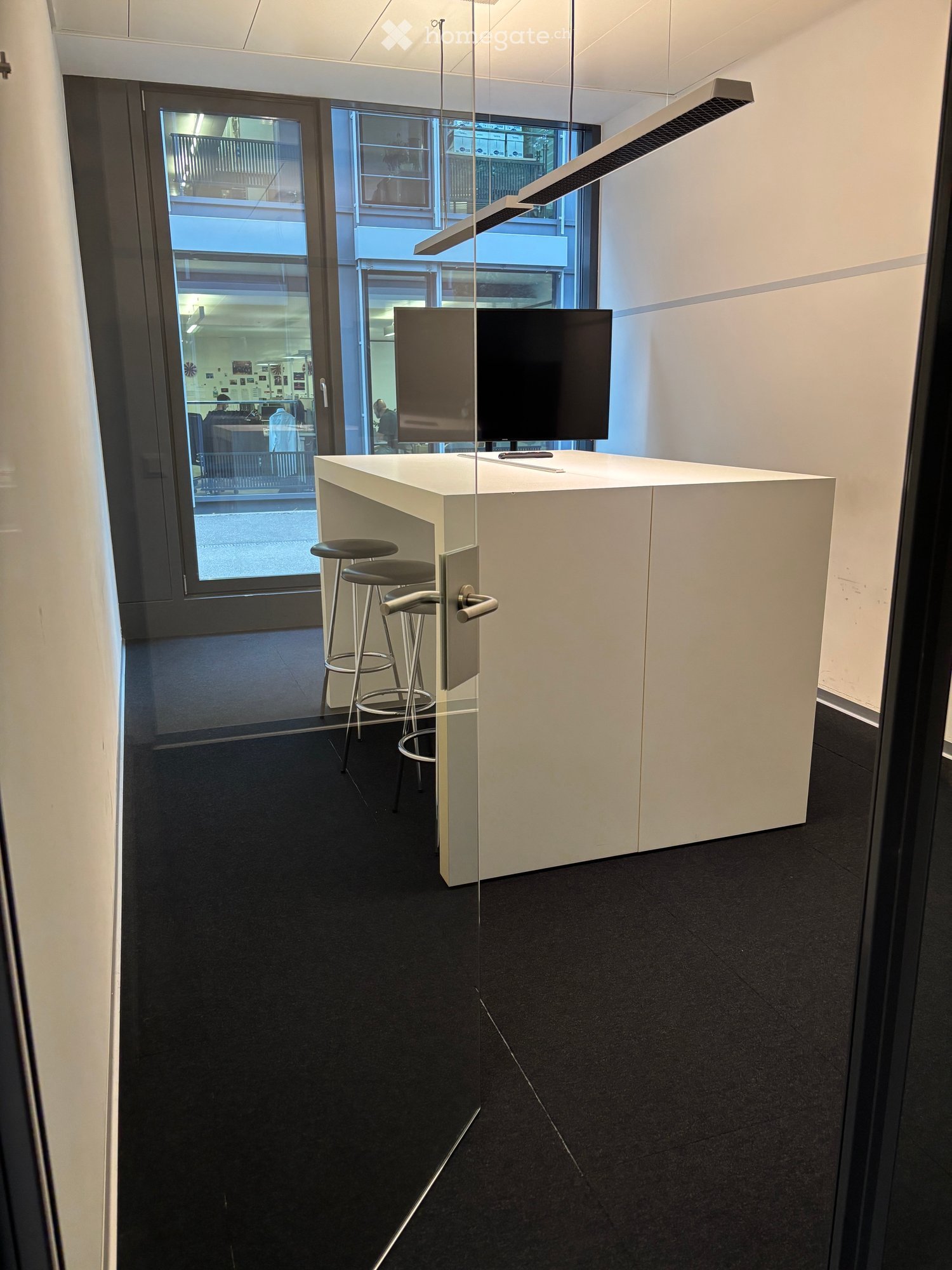 Modern reception area with a white reception desk, two black stools, a large screen, and a sleek glass partition.