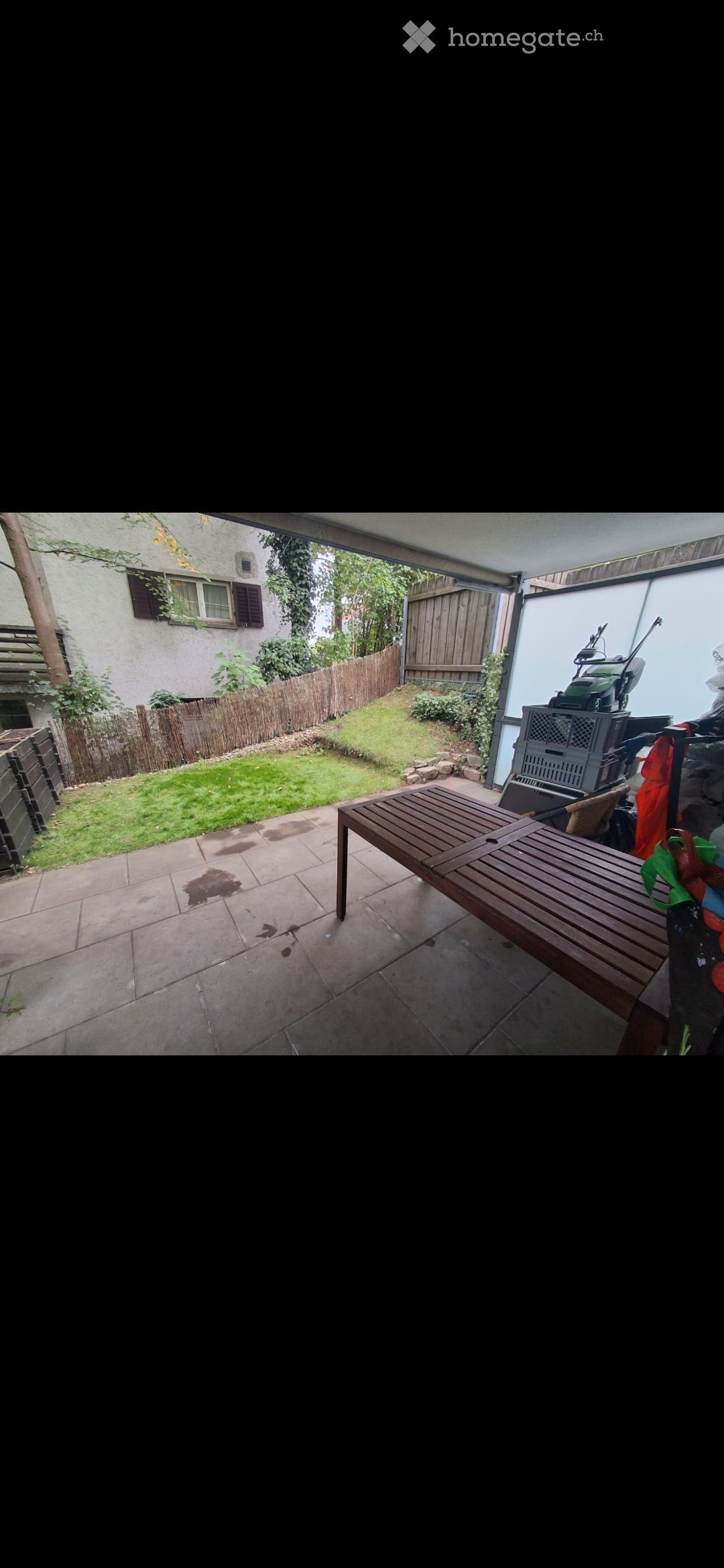 Patio area with tiled floor, wooden bench, grassy lawn, wooden fence, and neighboring house visible.