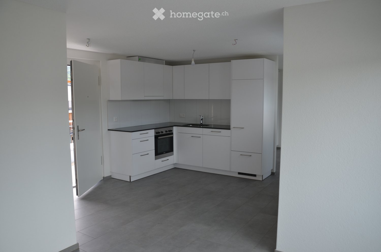 Modern kitchen with white cabinets, black countertops, and a built-in oven. The space features a dark tiled floor and a visible doorway leading to another room.