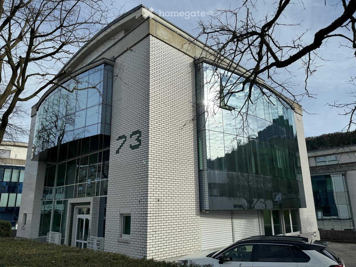 Modern two-story building with white brick facade and large glass windows, featuring the number "23" prominently displayed on the front.