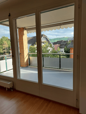 Balcony with white floor, metal railing, and view of houses and greenery.