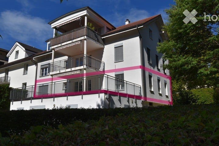 Two-story house with white exterior, pink trim, multiple balconies, and a well-maintained garden.
