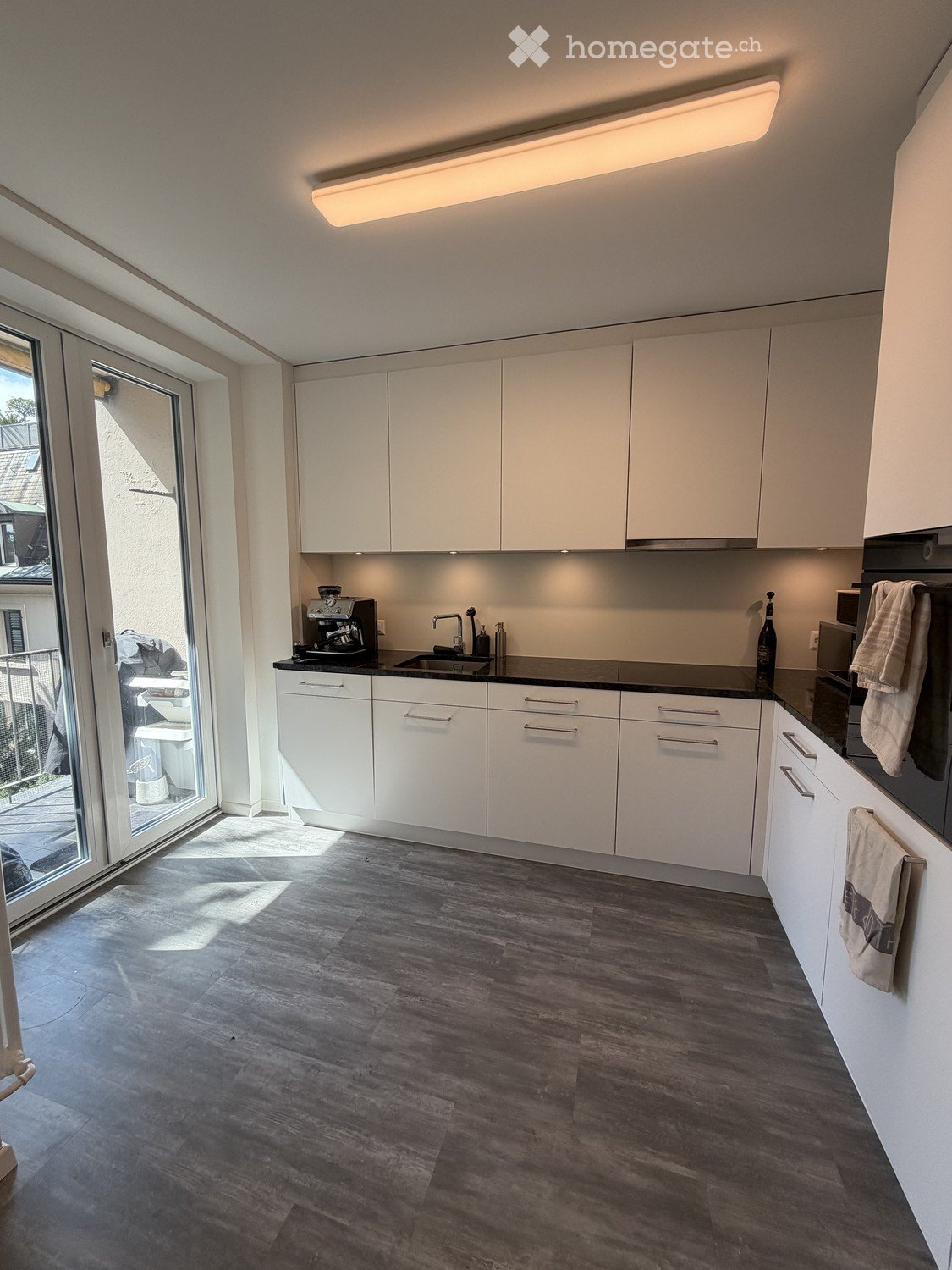 Modern kitchen with white cabinets, dark countertops, and wooden flooring. Features a coffee maker, sink, and oven.