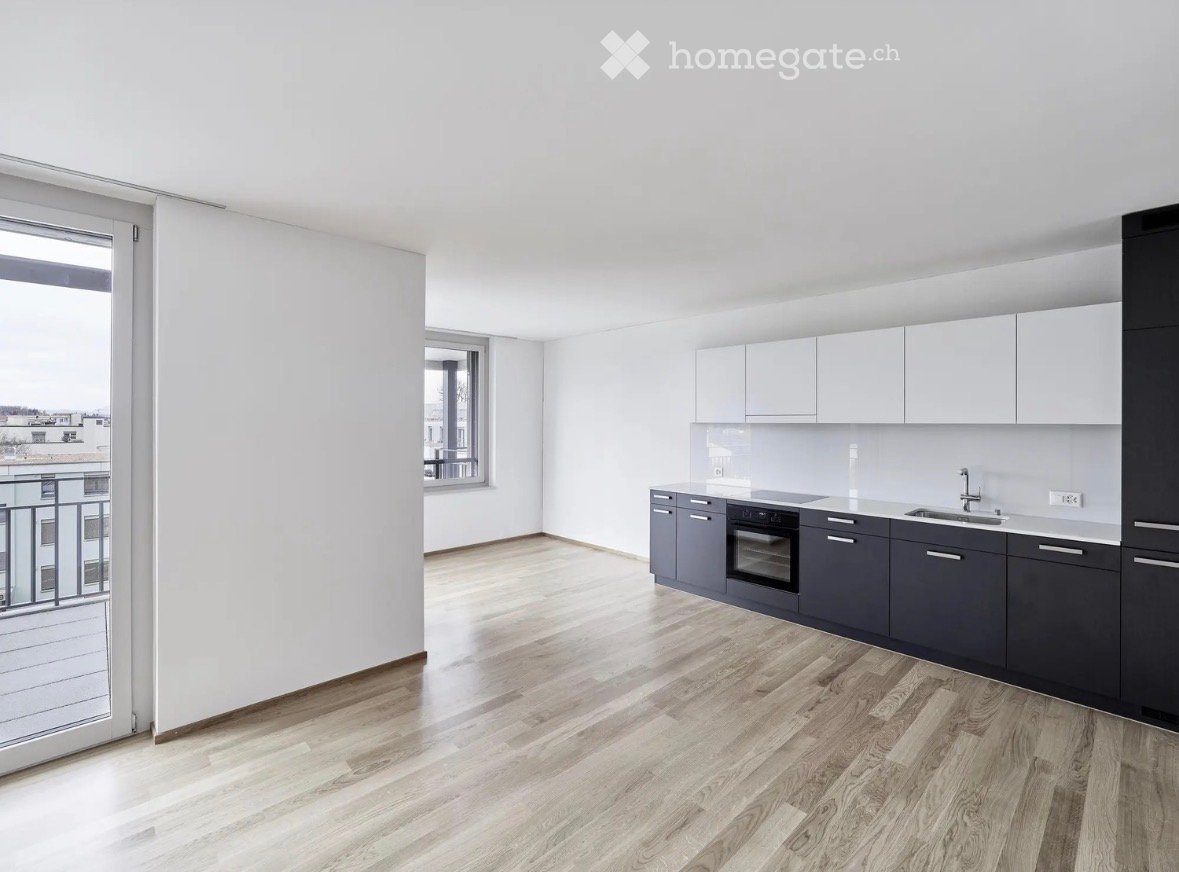 Modern kitchen with light wooden flooring, white walls, grey cabinets, and a built-in oven. Features a balcony with a view.