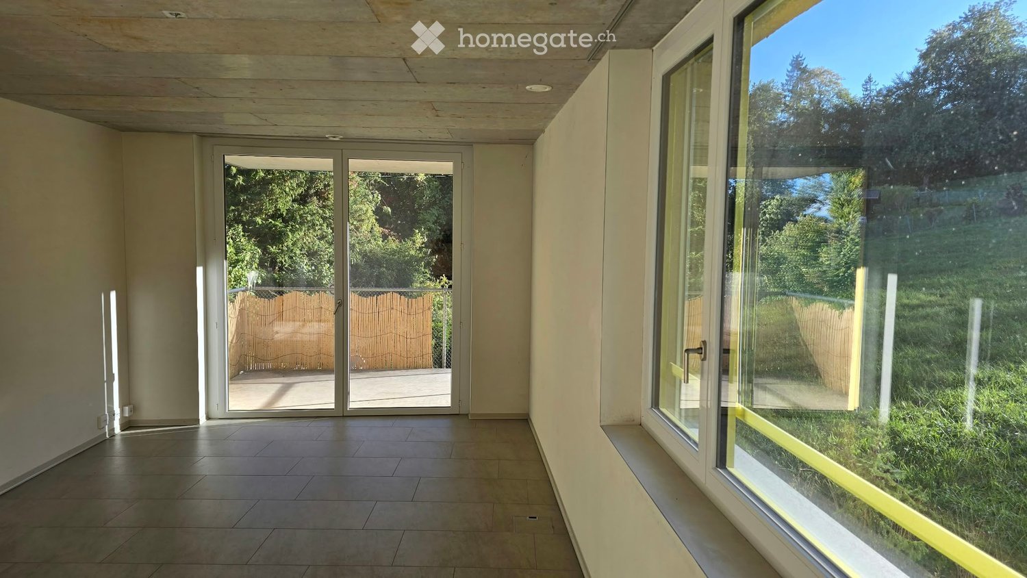 Empty room with tiled floor, large glass doors leading to an outdoor area, and natural light from windows.