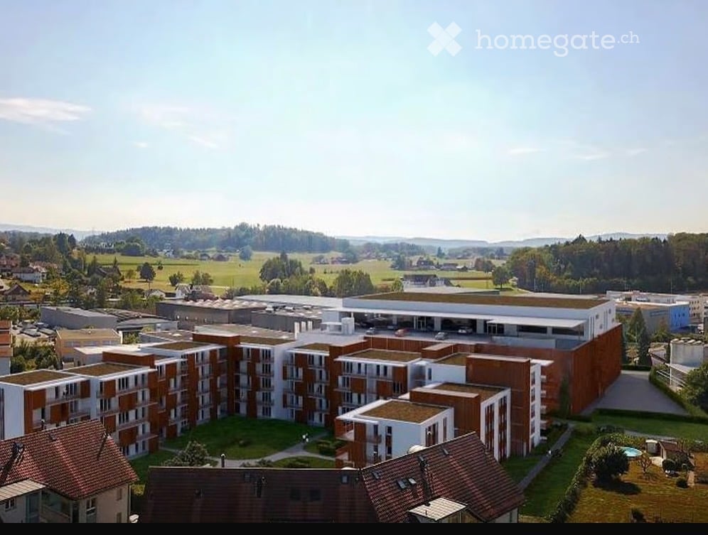 Aerial view of a modern residential complex with multiple apartment buildings, surrounded by green spaces and a parking area.