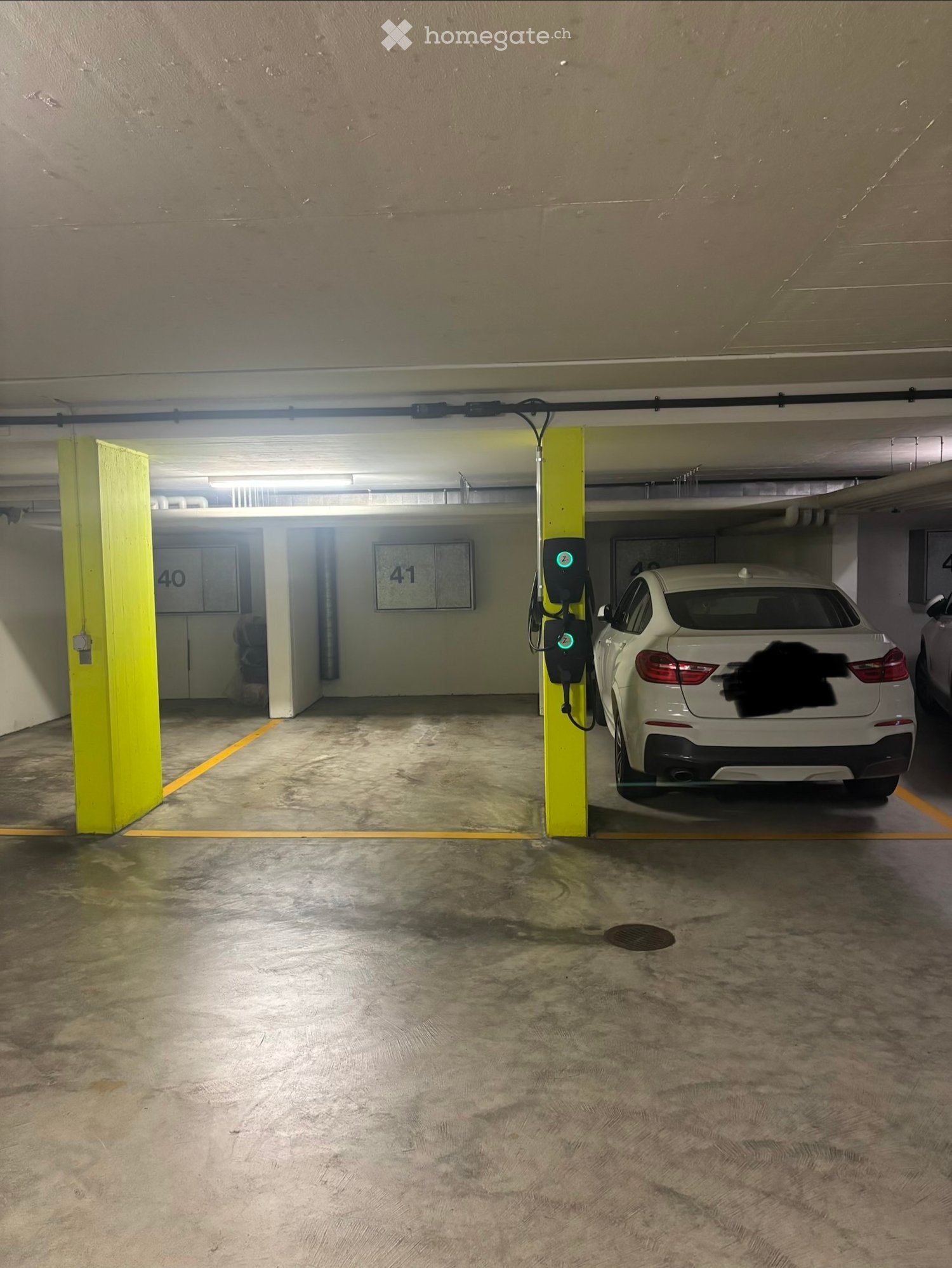 Underground parking area with concrete floors, yellow pillars, numbered parking spaces, and an electric vehicle charging station.