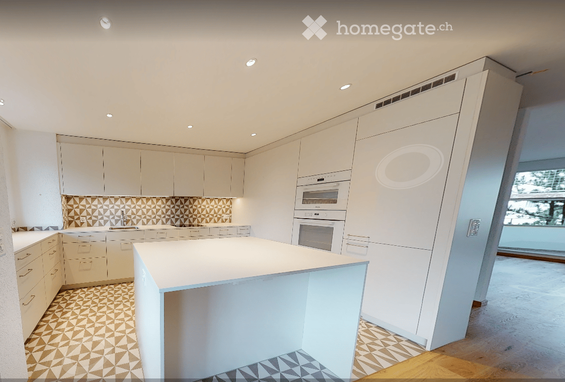 Modern kitchen with white cabinets, a central island, and built-in ovens. The backsplash features a geometric pattern, and the floor has a mix of wood and tile.