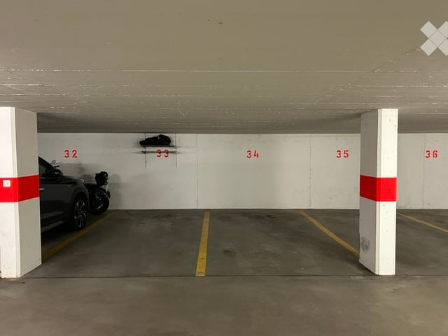 Underground parking area with numbered spots, white walls, and a parked car in one of the spaces.