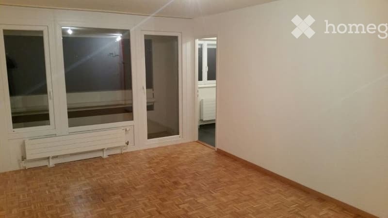 Empty room with wooden flooring, large windows, and a radiator. No furniture or equipment present.