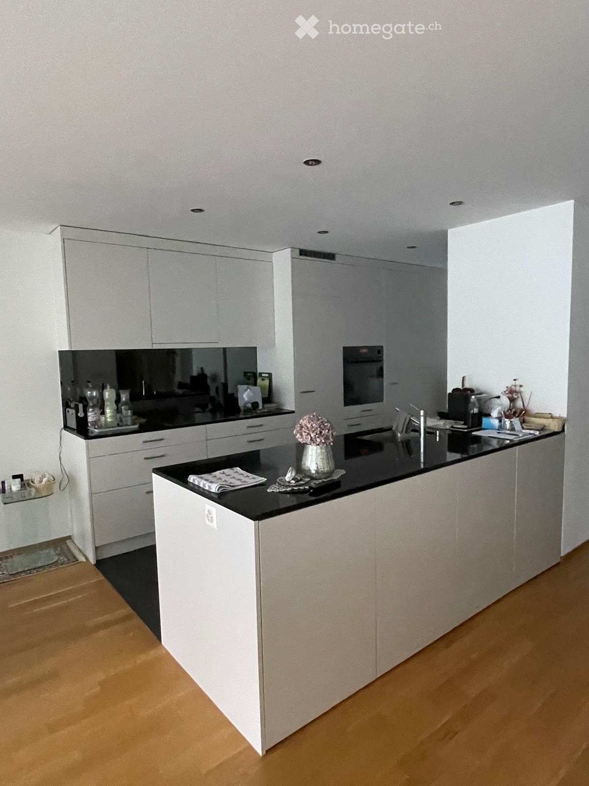 Modern kitchen with white cabinets, black countertops, and a central island. Features include a sink, faucet, oven, and decorative vase on the island.