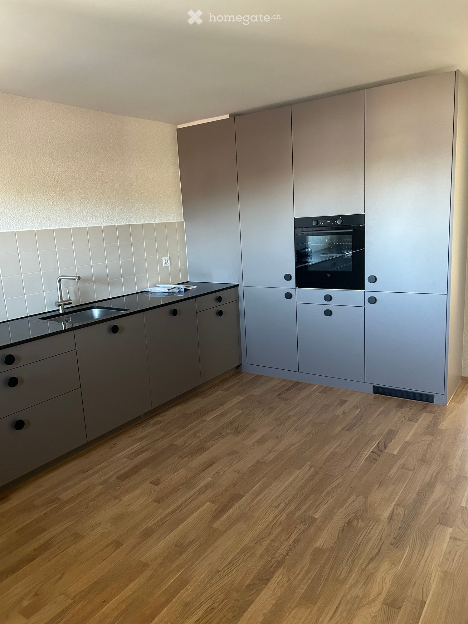 Modern kitchen with light grey cabinets, wooden flooring, and stainless steel sink and oven.