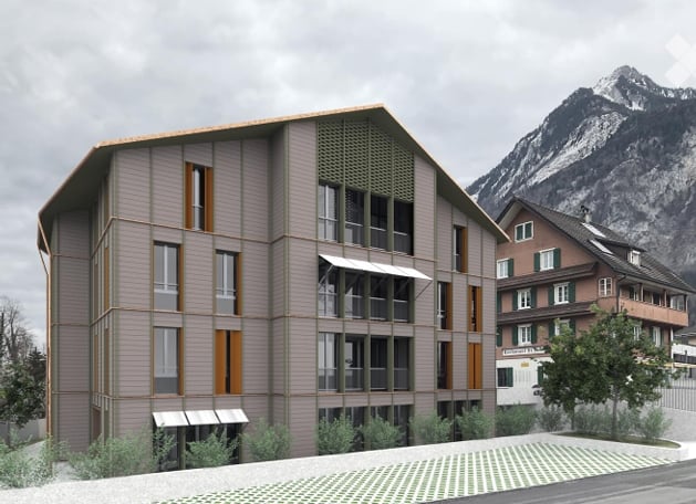 Modern multi-story building with large windows and a balcony, situated in a scenic area with mountains in the background.