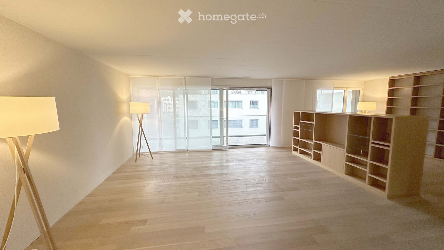 Empty room with wooden flooring, large glass sliding doors, built-in shelving unit, and floor lamps.