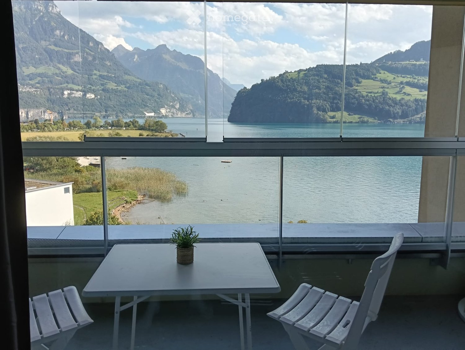 Balcony with a scenic mountain and lake view, featuring a small table, chairs, and a potted plant.