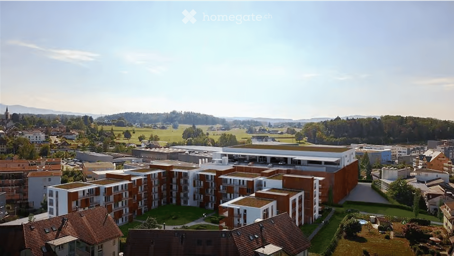 Aerial view of a modern residential complex with multiple buildings, surrounded by green spaces and a rural landscape.