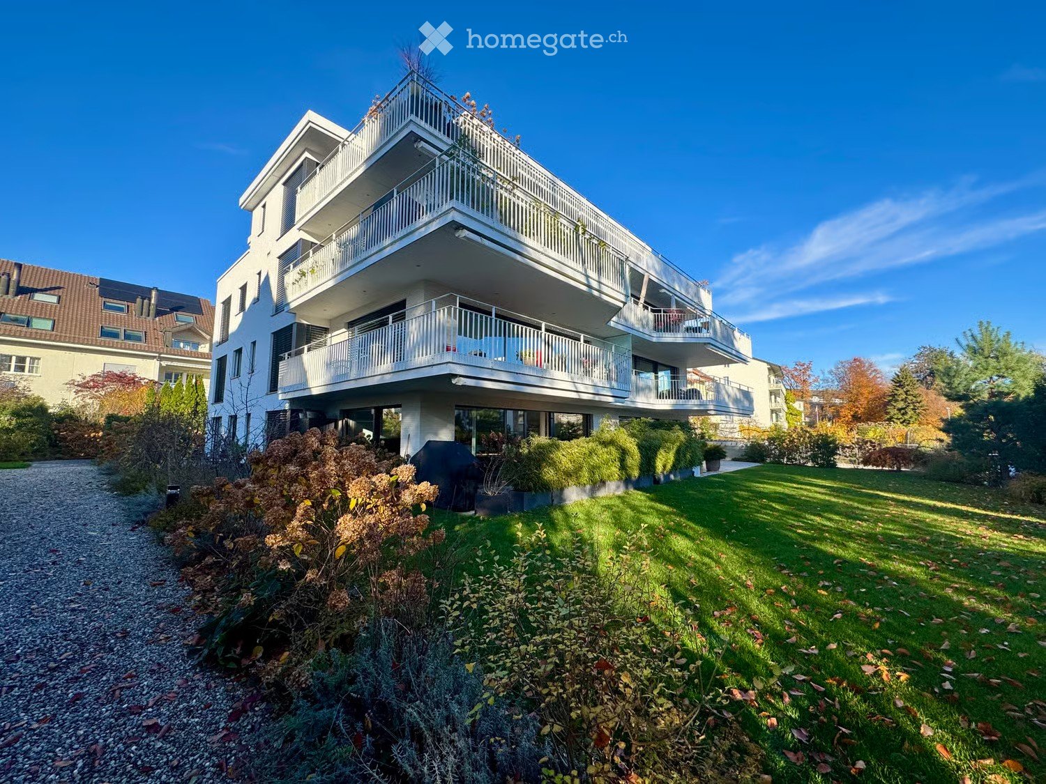 Modern two-story house with white exterior, multiple balconies, and a well-maintained garden.