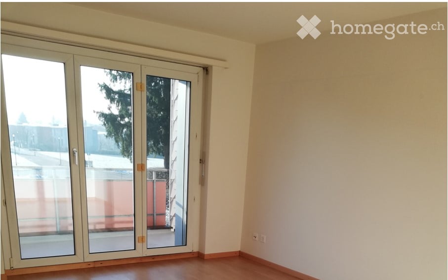 Empty room with wooden flooring, white walls, and large glass sliding doors leading to a balcony or outdoor area.